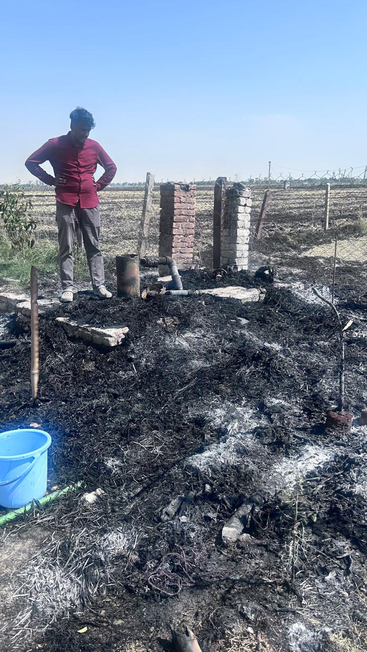 The burned-out tubewell area, brick pillars standing in ash, pipes and a blue bucket visible